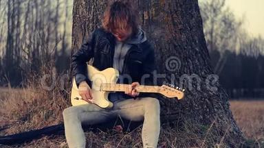 男音乐家坐在橡树下，日落时弹吉他